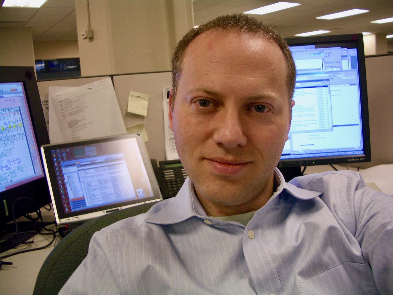 Lawrence Sinclair an seinem Schreibtisch bei Morgan Stanley, lächelnd in die Kamera, hinter ihm SAS auf den Bildschirmen